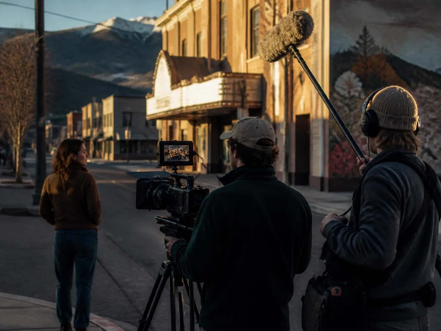 Film crew with a digital cinema camera and boom microphone shooting on a historic Western Colorado main street at golden hour