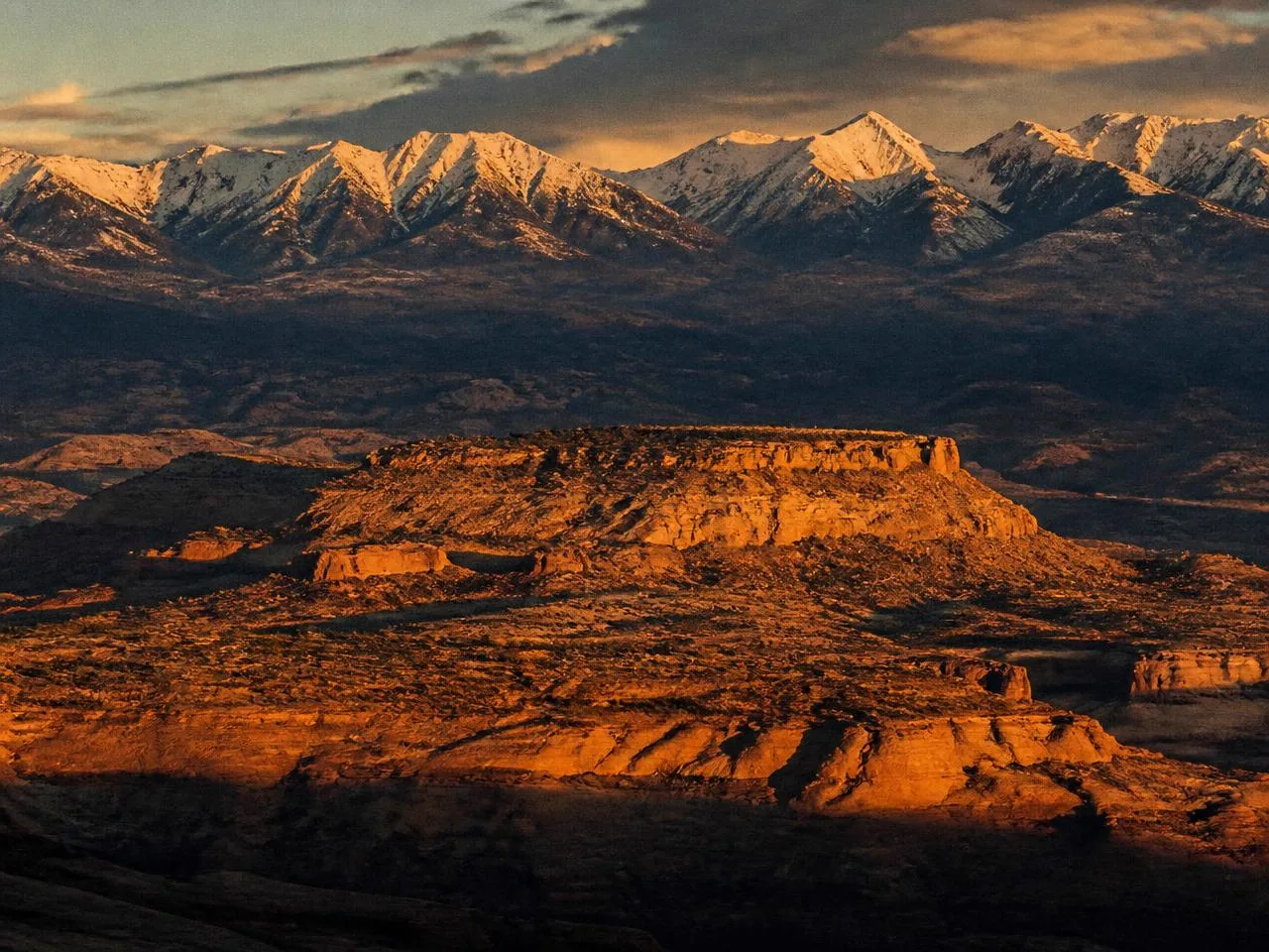 Snow-capped Western Colorado mountains rising above high desert mesas at golden hour